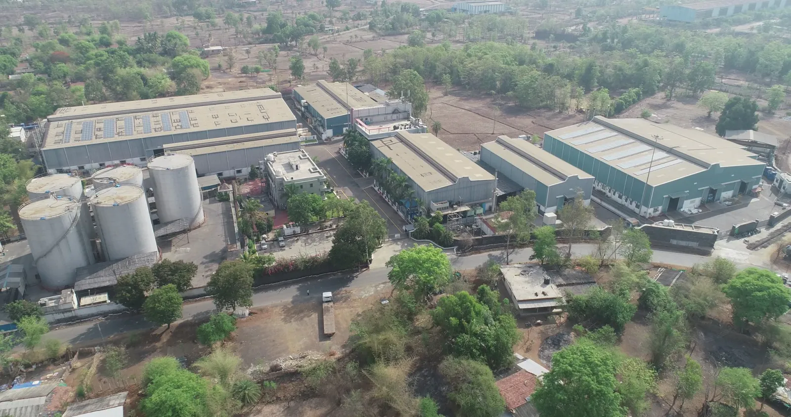 Aerial drone view of an industrial campus with storage silos, factory sheds and surrounding trees