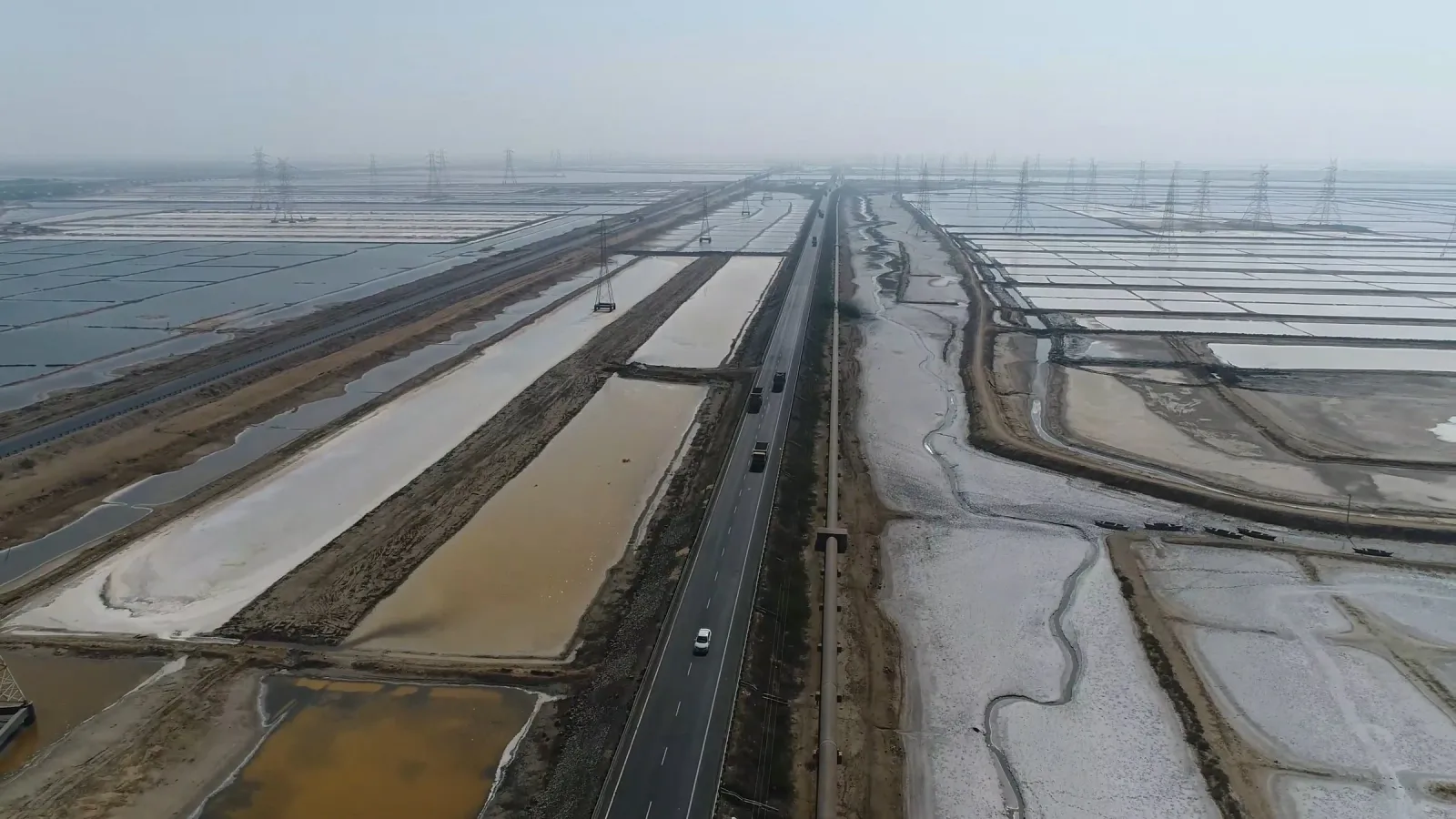 Aerial view of a highway and pipeline crossing salt pans lined with power pylons