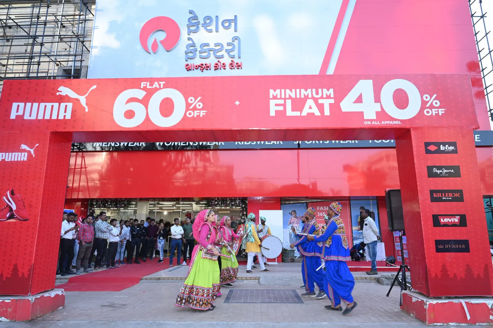 Folk dancers in colourful costumes perform at a retail store launch under a red entrance arch