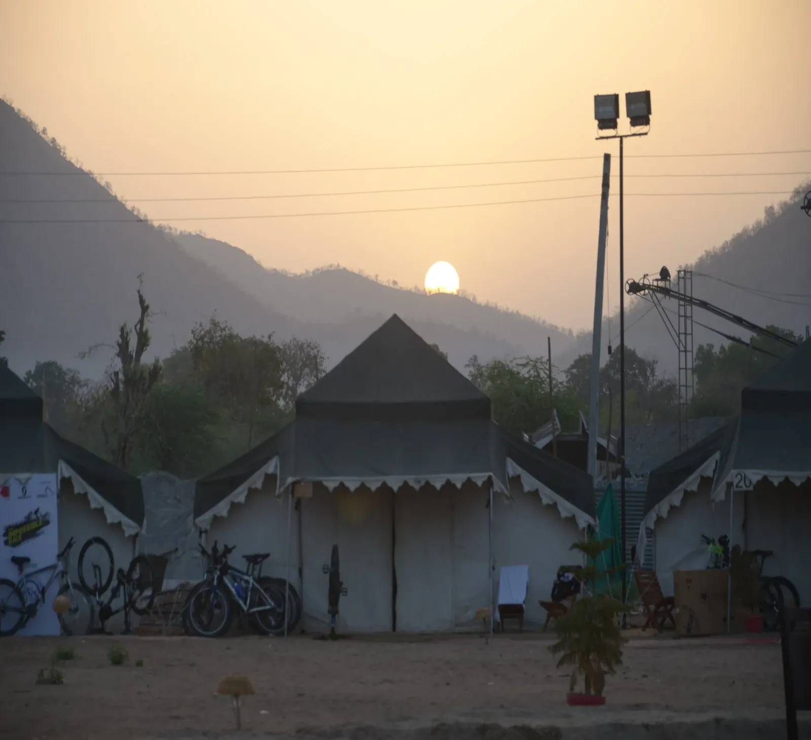 Sun rising over hills behind an event tent camp with mountain bikes parked outside
