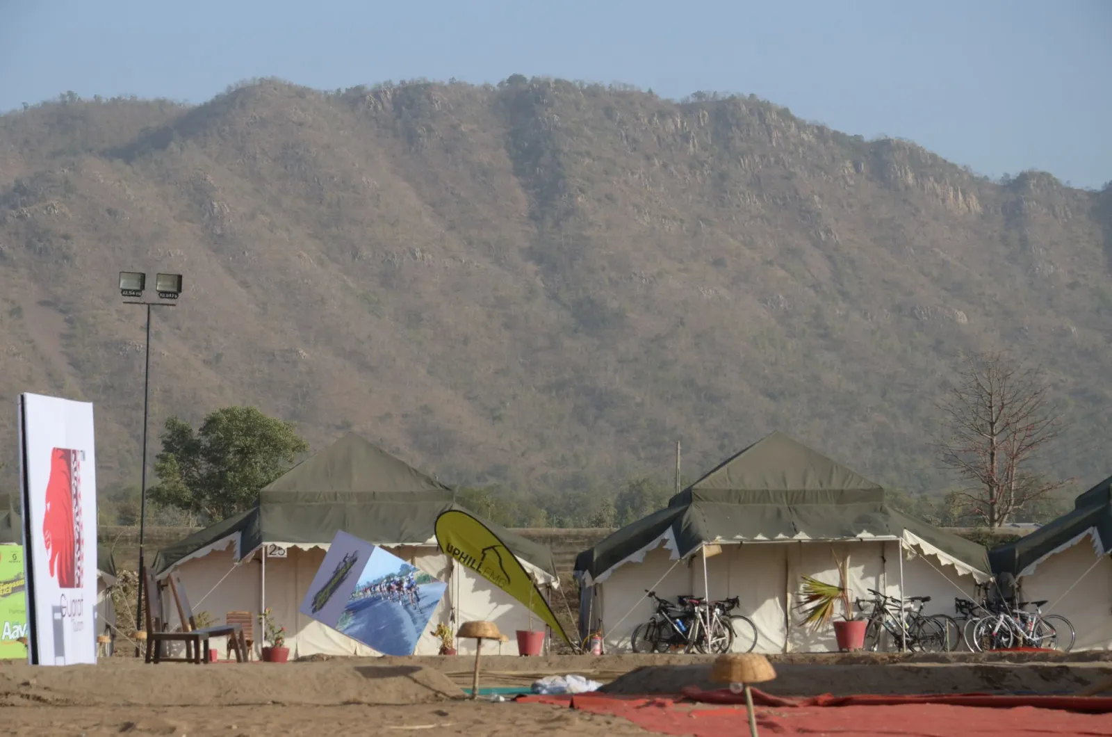 Event tent camp with parked bicycles and sponsor banners at the foot of a rocky hill