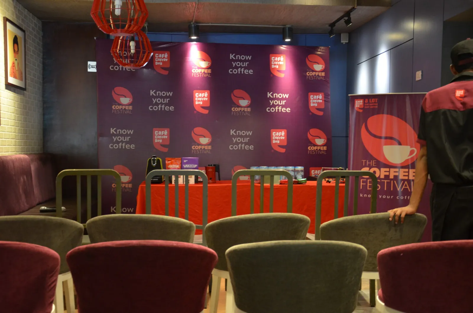 Rows of empty cafe chairs facing the Coffee Festival display table and backdrop before the session