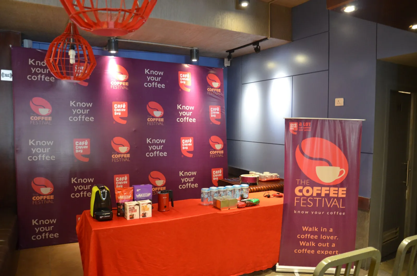 Coffee Festival stall with a roll-up standee, coffee machine and cups on a red table against a purple backdrop