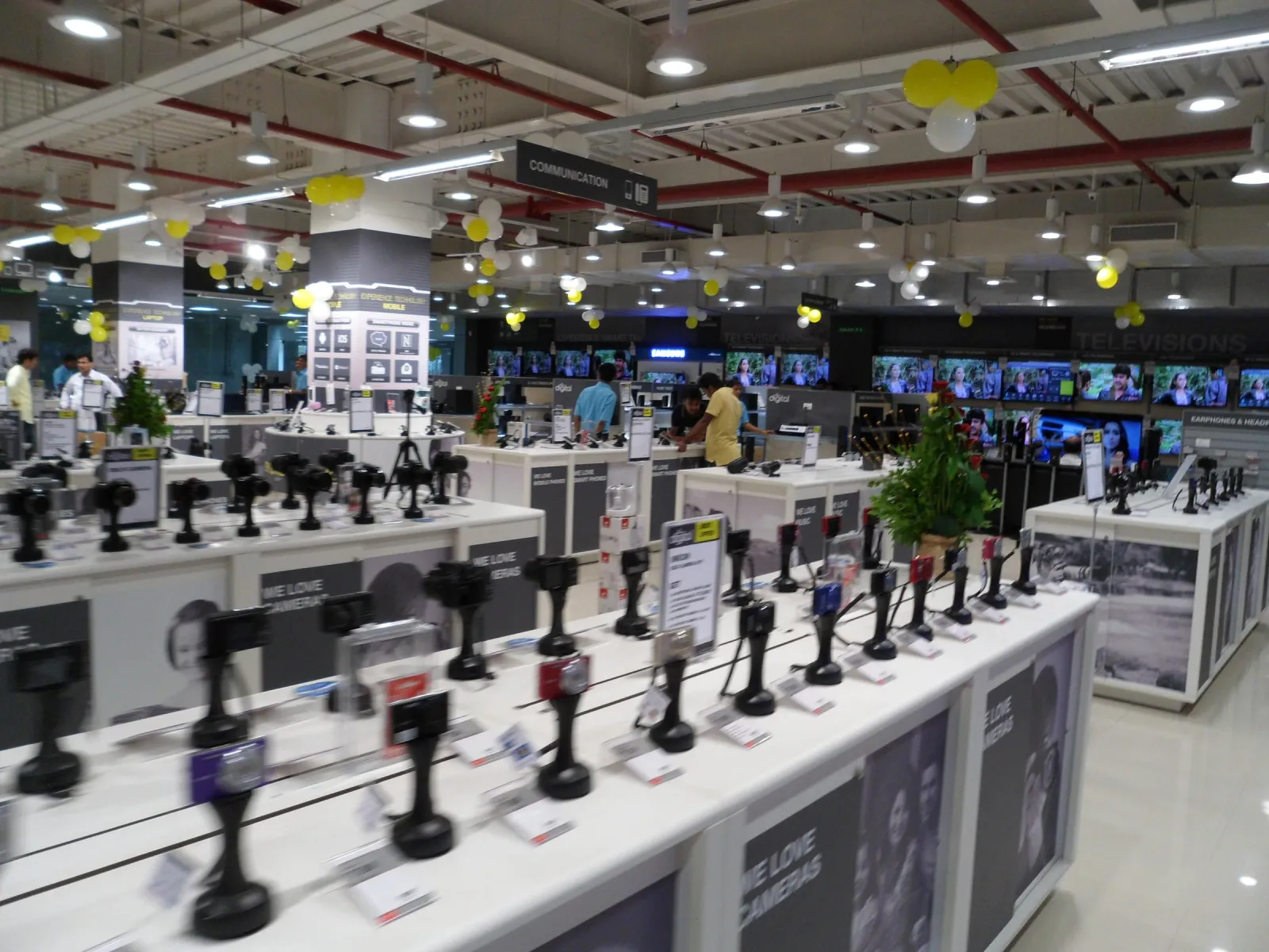 Camera display counter inside an electronics store decorated with yellow and white balloons for the opening