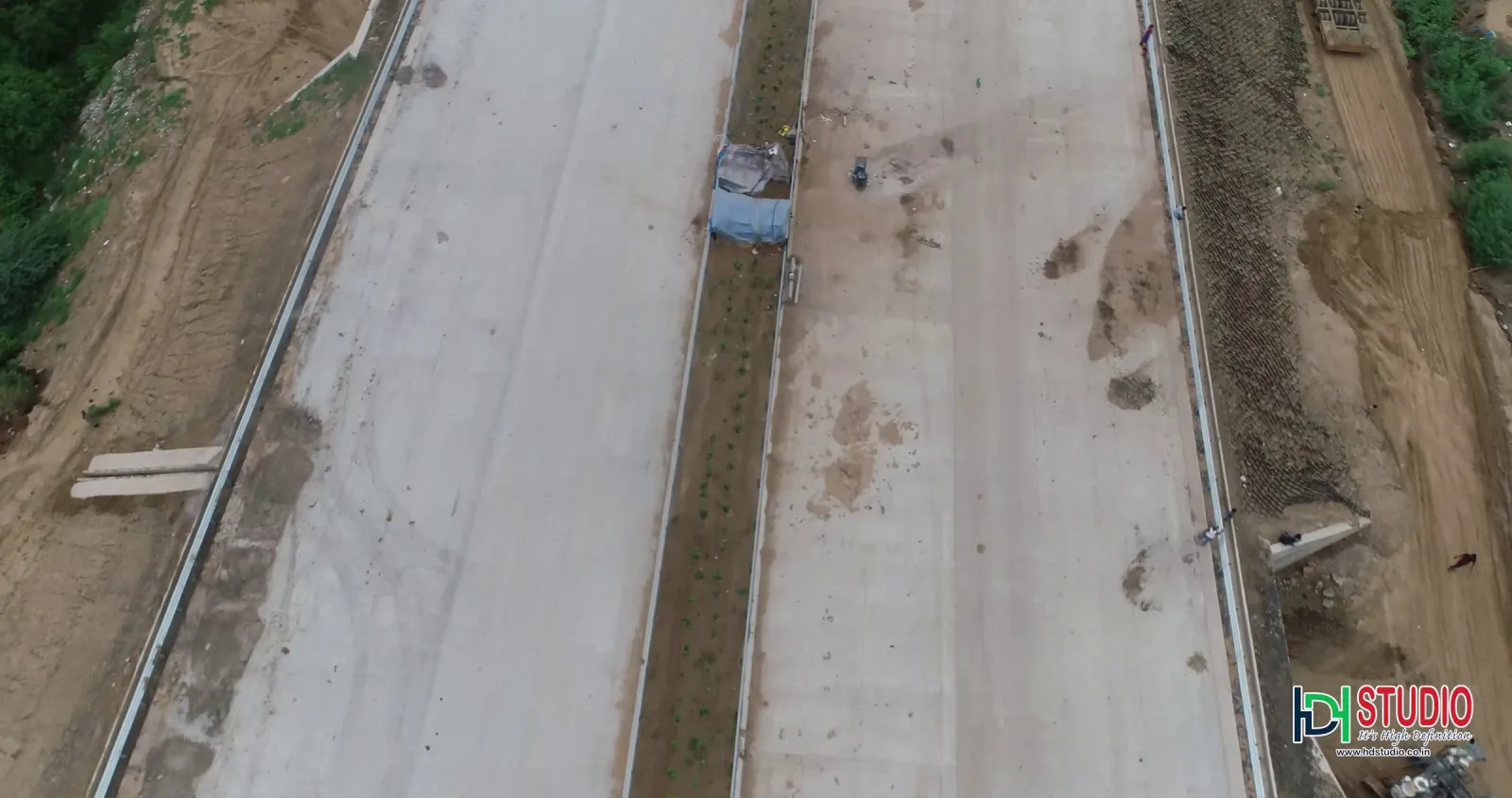 Aerial view of a new concrete highway under construction with a planted median and a truck on the carriageway