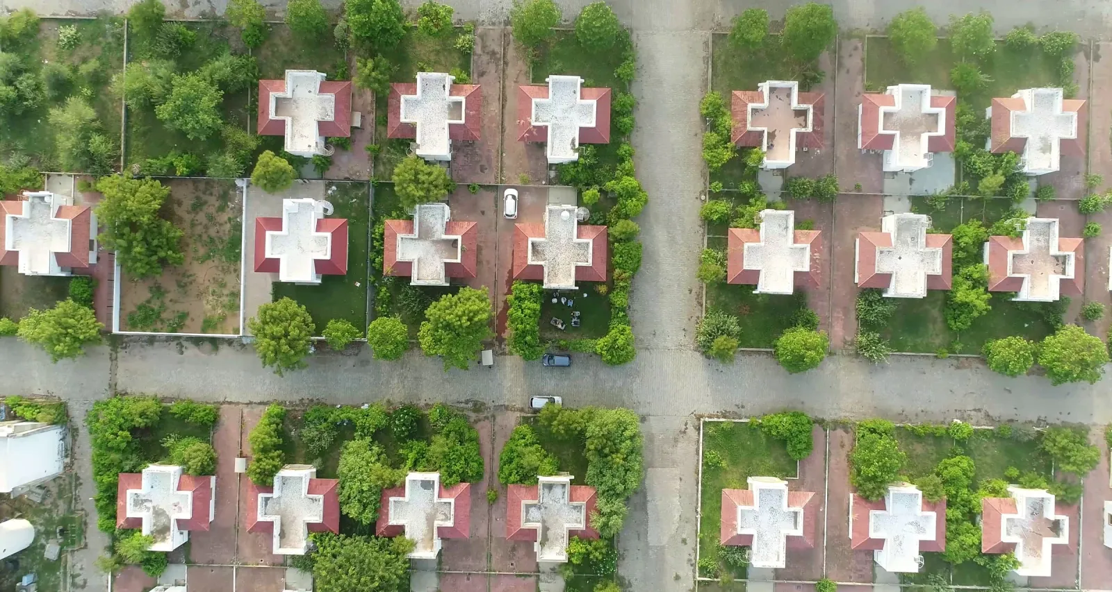 Aerial view straight down on rows of bungalows with red-tiled cross-shaped roofs, lawns and trees