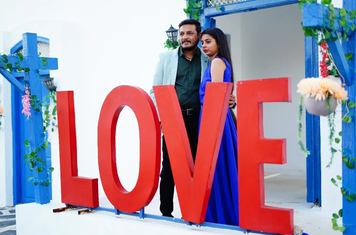 Couple poses behind giant red LOVE letters on a white and blue set during a pre-wedding shoot