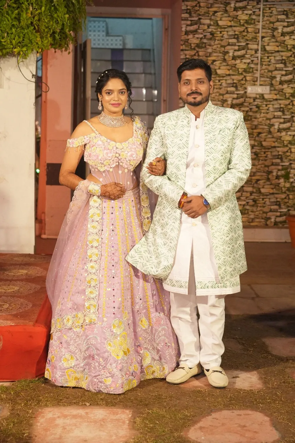 Bride in a lilac embroidered lehenga and groom in a printed sherwani pose together at an evening event